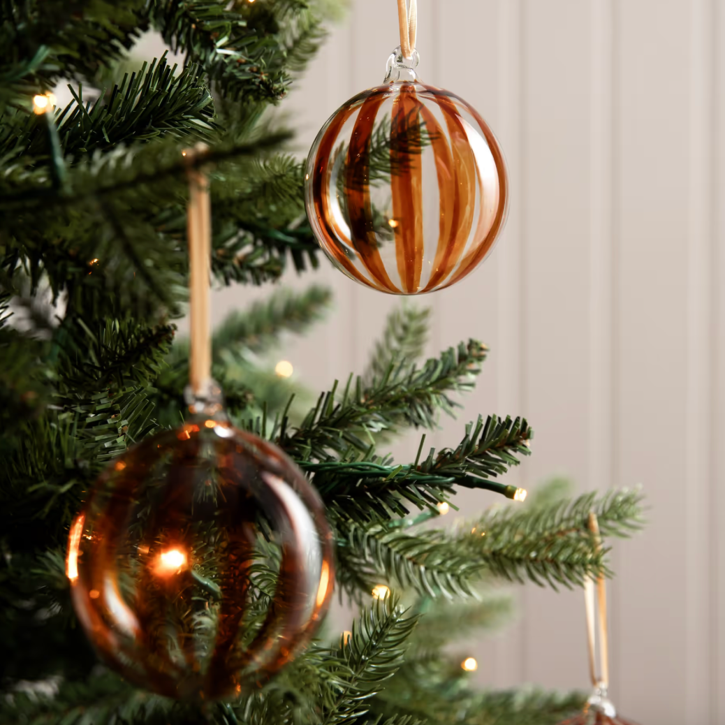 Two glass ornaments with striped pattern hanging on a Christmas tree.